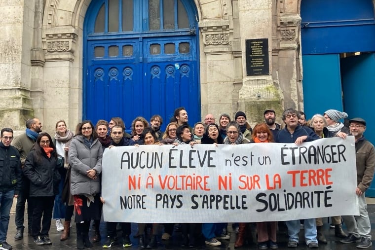 30 employés d'écoles à Paris France derrière une banderole opposée à la nouvelle loi anti-migrants